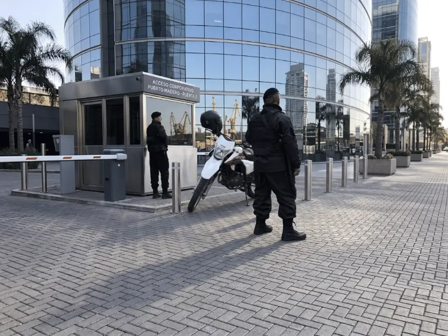 Dos vigiladores de GSP custodiando el acceso corporativo de un edificio de Puerto Madero, CABA, con garita, barrera y moto de patrullaje